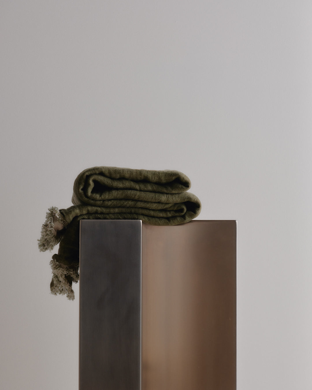 Folded green blanket on a metallic stand against a plain background
